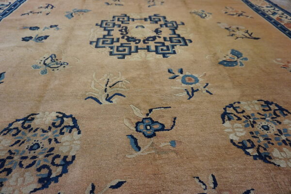 Beige field rug with scattered motifs in navy, light blue, and cream, featuring a prominent geometric key pattern.