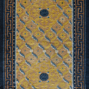 A gold patterned rug with central blue medallions and a wide navy border featuring a peach key design.