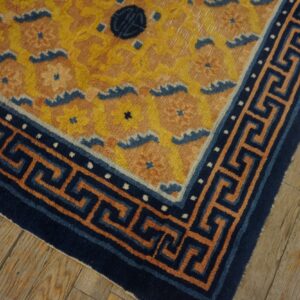 Yellow floral rug corner featuring a navy blue meander border rests on rustic light brown wood flooring.