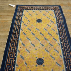 Yellow rug featuring blue medallions and a navy Greek key border, lying on distressed wood planks.