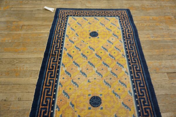 Yellow rug featuring blue medallions and a navy greek key border, lying on distressed wood planks.