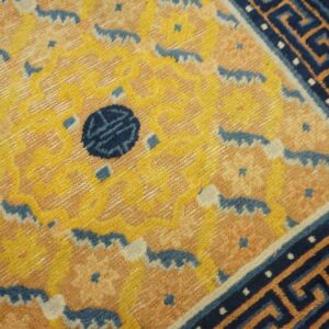 High-pile rug featuring a yellow and salmon pattern, a dark blue medallion, and a striking Greek key border.