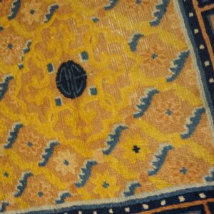 Textured rug detail in gold, tan, and navy blue with stylized floral and meander designs.