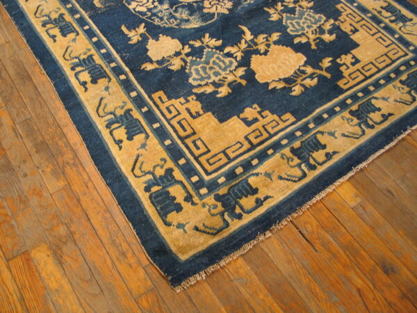 Blue and gold patterned rug with floral and geometric motifs rests on rustic hardwood flooring.