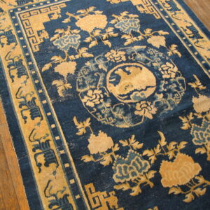 Traditional blue and gold rug with floral patterns and a central medallion on wood plank flooring.