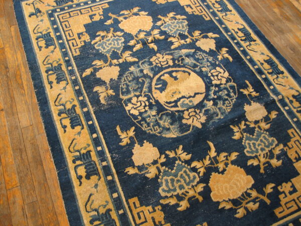Traditional blue and gold rug with floral patterns and a central medallion on wood plank flooring.