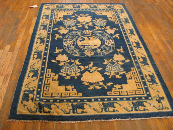 Rectangular blue and tan patterned rug with thick borders displayed on polished hardwood flooring.