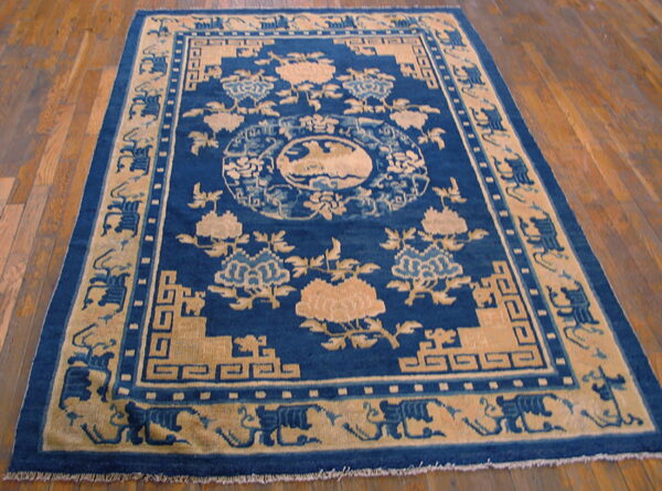 Deep blue and tan rug with an ornate floral and geometric pattern on a polished wood floor.