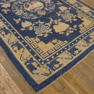 Blue and tan rug with intricate floral and geometric patterns rests on wide plank wood floors.