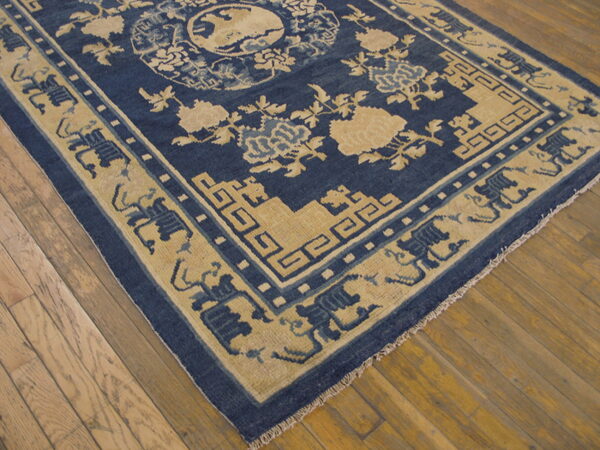Blue and tan rug with intricate floral and geometric patterns rests on wide plank wood floors.