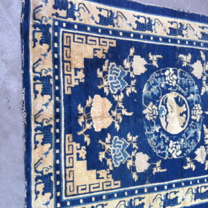Blue rug with cream floral patterns and intricate geometric key borders on a gray concrete floor.