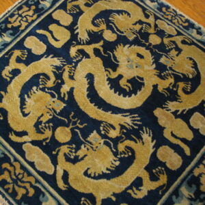A dark blue rug featuring a large gold and teal mythical dragon pattern rests on a hardwood floor.