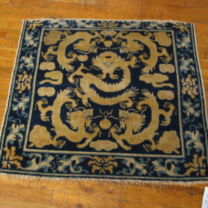 A square, dark blue rug with large golden dragon patterns rests on glossy wood flooring.
