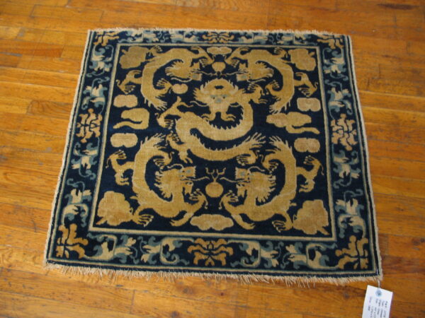 A square, dark blue rug with large golden dragon patterns rests on glossy wood flooring.
