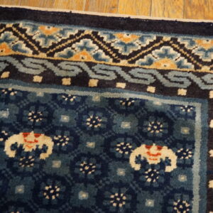 Dark blue patterned rug corner with cream, orange, and light blue borders rests on hardwood flooring.