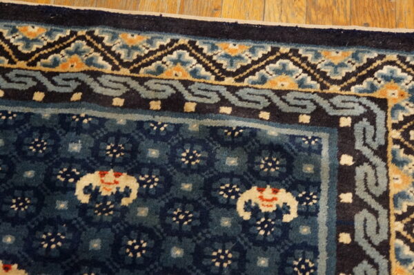 Dark blue patterned rug corner with cream, orange, and light blue borders rests on hardwood flooring.