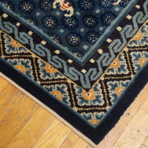 Close-up of a navy and teal geometric rug corner with orange accents on rustic light wood planks.