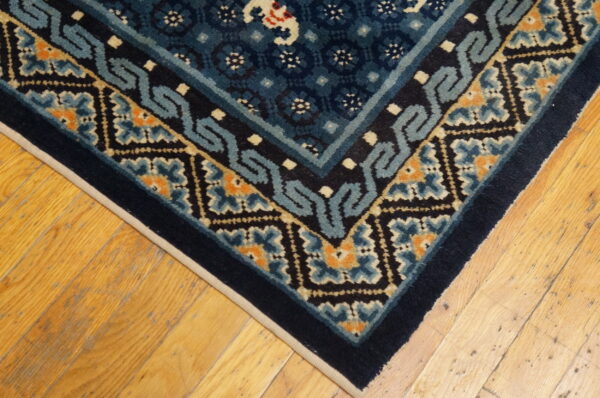 Close-up of a navy and teal geometric rug corner with orange accents on rustic light wood planks.