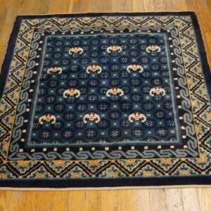 Square navy blue rug with complex borders in light blue, cream, and orange on a wood floor.