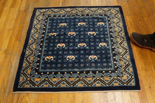 Square navy blue rug with complex borders in light blue, cream, and orange on a wood floor.