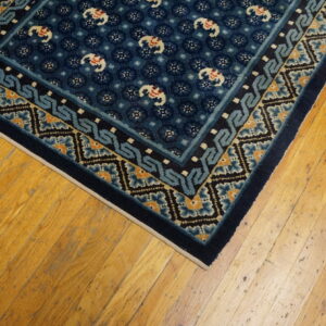 Dark blue rug with white elephant motifs and borders of light blue and orange rests on wood flooring.