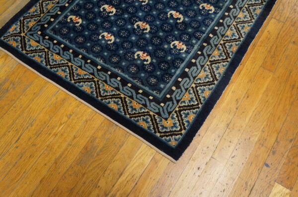 Dark blue rug with white elephant motifs and borders of light blue and orange rests on wood flooring.