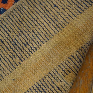 A rolled rug shows tan ribbed texture with navy stripes over distressed orange wood floorboards.