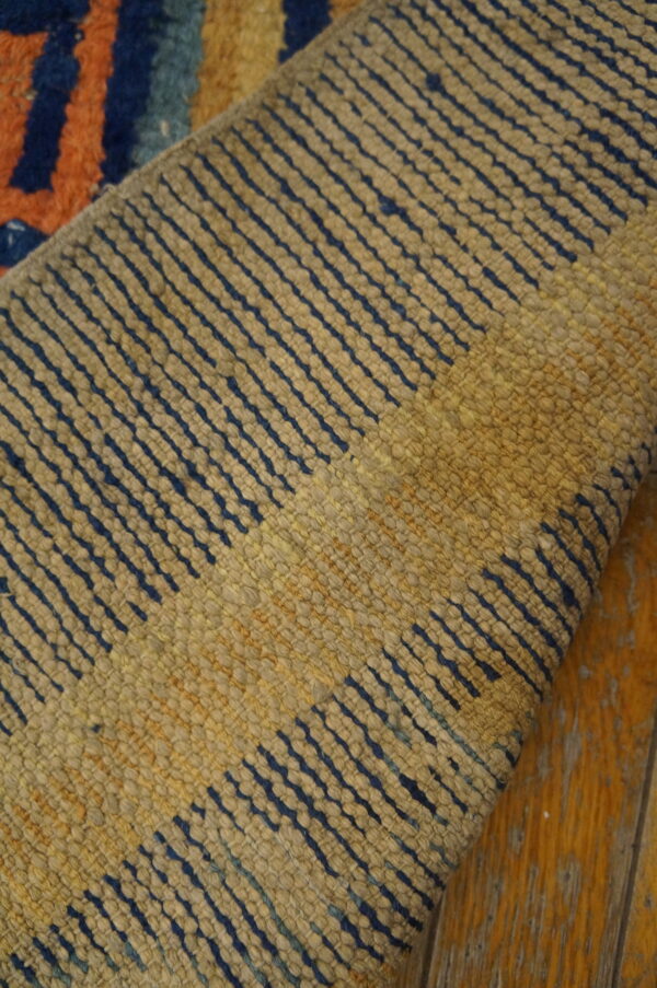 A rolled rug shows tan ribbed texture with navy stripes over distressed orange wood floorboards.
