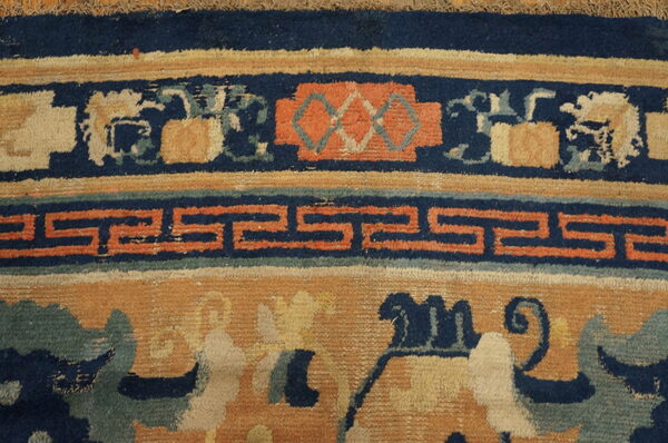 Detailed view of a rug with navy, rust, and gold border featuring fretwork and floral motifs.