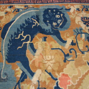Close view of a rug with a dark blue animal pattern set against an orange, cream, and coral floral field.