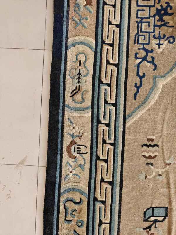 High-pile tan rug border featuring navy, light blue, and beige key patterns rests on white tiled floor.