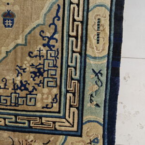 Close-up showing a beige rug with dark blue geometric and stylized aquatic patterns on white tile.