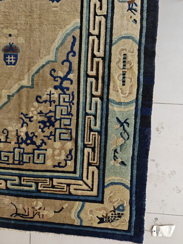 Close-up showing a beige rug with dark blue geometric and stylized aquatic patterns on white tile.