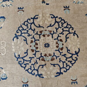Low-pile beige rug with a prominent blue scroll medallion and scattered light blue and brown designs.