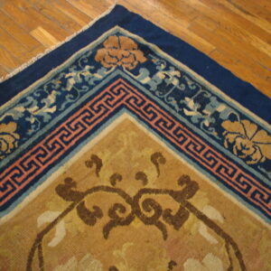 Tan, blue, and coral rug border featuring floral and Greek key patterns rests on light brown hardwood floors.