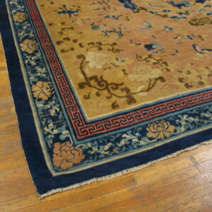 Tan field rug with scattered floral and blue motifs, framed by a dark blue ornamental border on wood flooring.