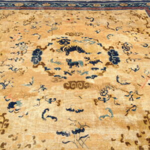 Worn gold and blue oriental rug featuring a central medallion with animal figures and elaborate decorative borders.