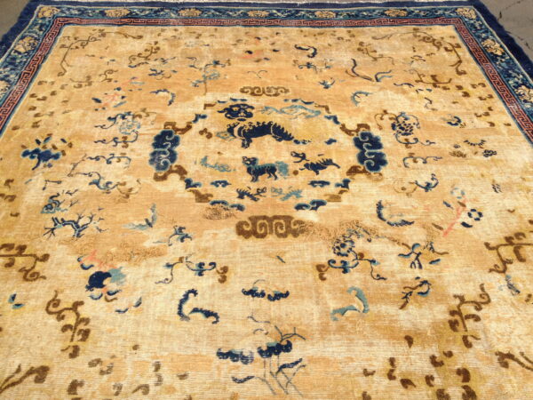 Worn gold and blue oriental rug featuring a central medallion with animal figures and elaborate decorative borders.