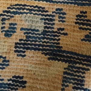 Detail of a low-pile rug featuring a stepped geometric pattern in dark blue, tan, and light green.