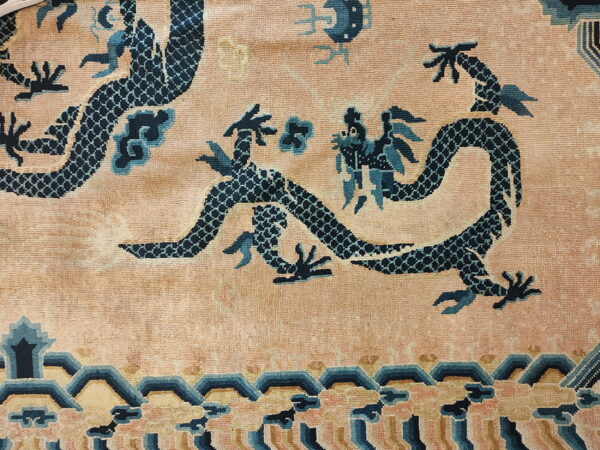 Low-pile peach rug featuring dark blue serpentine dragons and a tiered wave border.