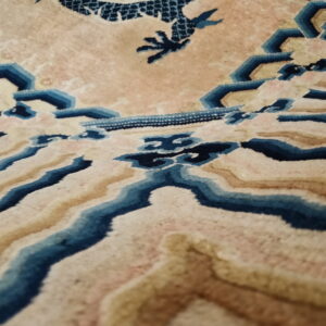 Detail view of a pale gold rug with blue and tan wavy patterns and a dark blue claw-like motif.