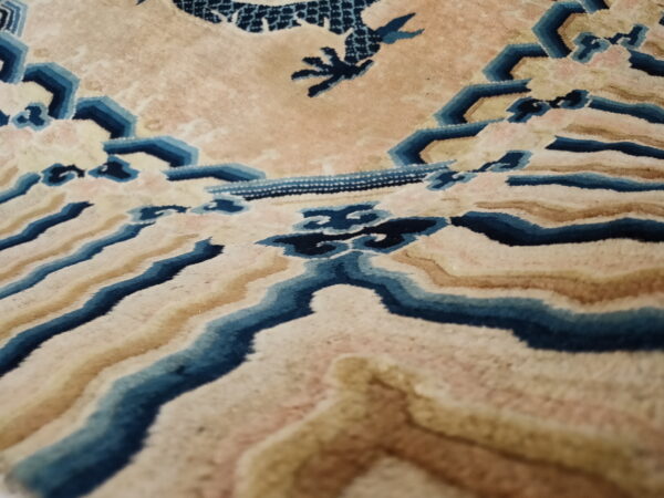 Detail view of a pale gold rug with blue and tan wavy patterns and a dark blue claw-like motif.