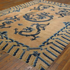 Large tan rug featuring prominent navy blue dragon designs rests on distressed hardwood flooring.