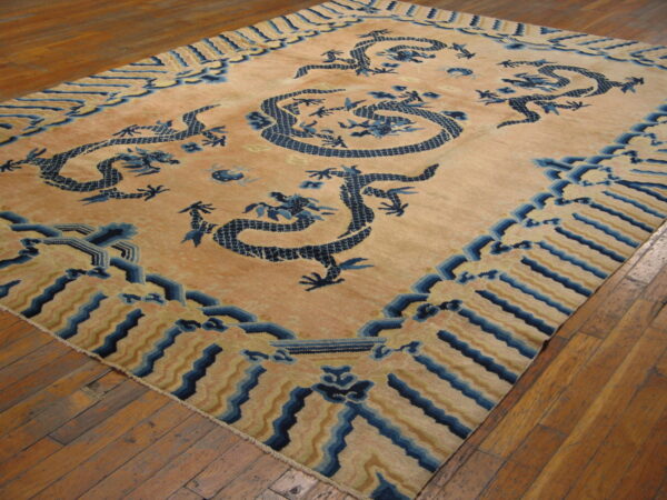 Large tan rug featuring prominent navy blue dragon designs rests on distressed hardwood flooring.