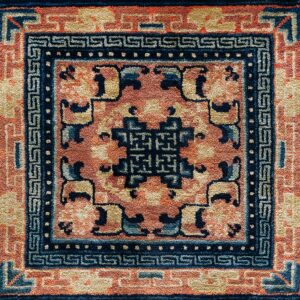 Textured rug detail with a navy geometric border and central medallion on a coral field.