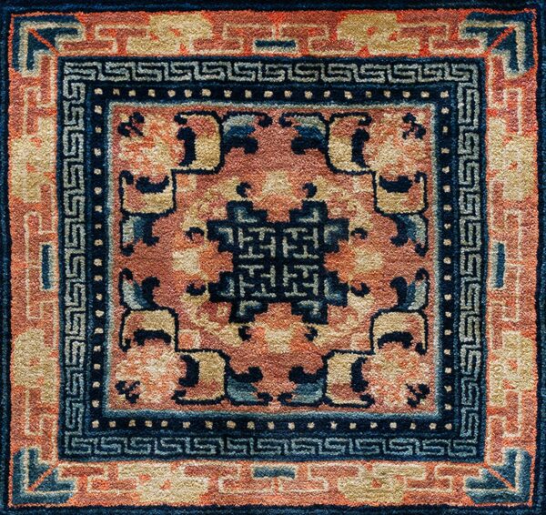 Textured rug detail with a navy geometric border and central medallion on a coral field.