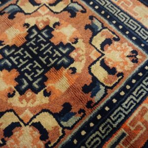 Navy, terracotta, and tan rug detail showing a complex geometric pattern and an intricate meander border.