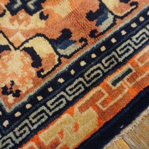 Close-up view of a rug corner featuring peach, navy, and tan colors with geometric borders on wood flooring.