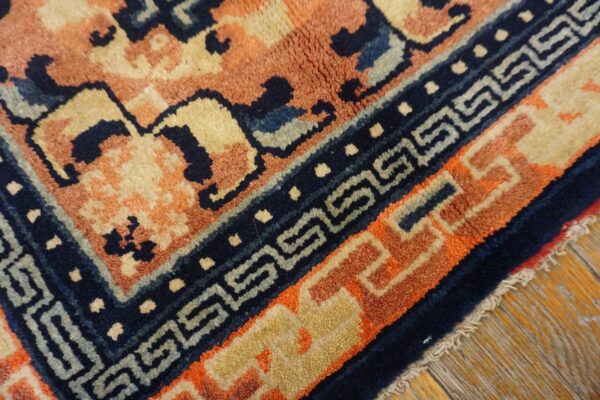 Close-up view of a rug corner featuring peach, navy, and tan colors with geometric borders on wood flooring.