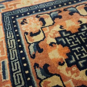 Close-up of a rug featuring deep blue, terracotta, and beige geometric patterns with a visible medium pile.